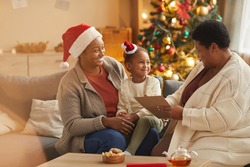 Warm-toned portrait of smiling African-American family reading letter to Santa with cute little girl while enjoying Christmas season at home