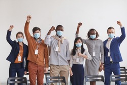 Multi-ethnic group of business people wearing masks and cheering while standing in row against white in conference room