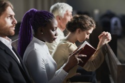 Group of people sitting on the bench in church and praying during ceremony
