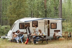 Wide angle view of young people enjoying outdoors while camping with van in forest, copy space
