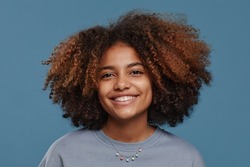 Front view portrait of young African-American woman with natural curly hair smiling happily at camera in studio against blue background
