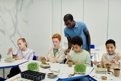 Diverse group of children planting seeds while experimenting at biology class in school with African-American teacher supervising