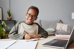 Portrait of smiling African-American boy wearing glasses while studying at home, homeschooling concept, copy space
