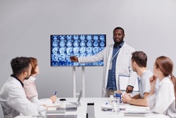 Contemporary medical expert or radiologist pointing at mri scan with x-ray images of human brain during consultation with colleagues