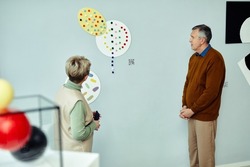 Senior Caucasian man and woman visiting contemporary art exhibition museum having discussion about unusual picture on wall