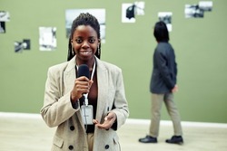 Horizontal medium portrait of young African American art gallery curator holding microphone speaking about current exhibition