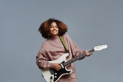 Minimal waist up portrat of curly haired black girl playing electric guitar and smiling at camera, copy space