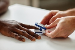 Close-up shot of unrecognizable doctor applying pulse oximeter on Black patients finger during appointment