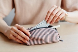 Minimal close up of young woman putting birth control pills in purse and other feminine essentials