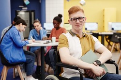 Vibrant portrait of red haired young man with disability in college library looking at camera, copy space