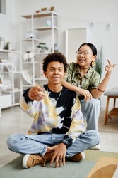 Vertical full length portrait of two gen Z teenagers boy and girl smiling at camera while posing in home interior