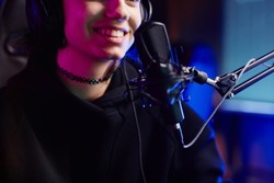 Close up of smiling young woman speaking to microphone in neon light while recording podcast or streaming gaming, copy space