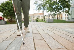 Low angle shot of blind man walking in city and using cane on pavement, copy space