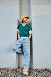 Vertical portrait of young Asian man wearing colorful street style clothes standing by concrete wall in urban setting