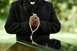 Close up of African American priest wearing black at outdoor funeral ceremony with focus on hands in prayer