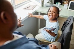 High angle portrait of black little girl screaming at father trying to take away smartphone 