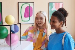 Colorful portrait of two teenage girls looking at abtract sculpture in modern art gallery