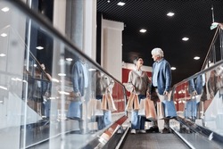 Front view of happy senior couple holding shopping bags standing on escalator in mall, copy space