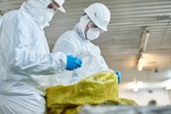 Side view portrait of two workers  wearing biohazard suits working at waste processing plant sorting recyclable plastic on conveyor belt