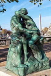 Bronze statue The Kiss (1882) by Auguste Rodin (1840-1917) in the Tuileries Garden, in front of the Orangerie museum, with Egyptian obelisk in background - Paris, France