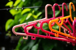 Colorful clothes hanger hanging with rain drop on green tree background.Rainy day concept.