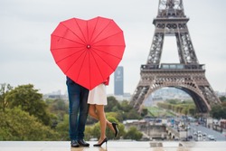 The couple hidden with red umbrella in front of the Eiffel tower in Paris