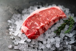 Raw fresh New York beef steak on ice with herbs and rosemary, close up