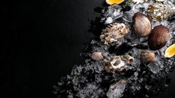 Raw Clams vongole shells, mussels, oysters and lemon with ice on black slate. Fresh shellfish for cooking with seasonings on the table, top view