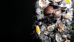 Raw Clams vongole shells, mussels, oysters and lemon with ice on black slate. Fresh shellfish for cooking with seasonings on the table, top view and copy space