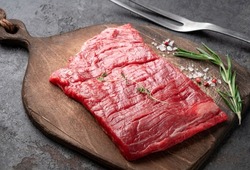 Raw flank steak or Outside skirt steak on a wooden board with grilling seasonings, close up