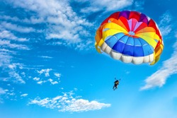 Two men are flying in the blue sky using a colorful parachute.