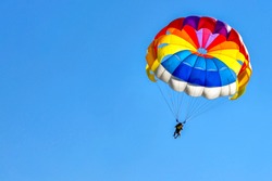 Two men are gliding using a parachute on the background of the blue sky.