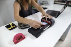 Clear image of female hand inserting  imprinting paper with credit card underneath into old pre-digital credit card imprinter machine white office table background 