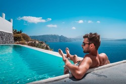 man relaxing in infinity swimming pool looking at the ocean,young man in the swimming pool relaxing looking out over the ocen caldera of Oia Santorini Greece