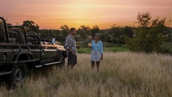 Asian women and European men on safari game drive in South Africa Kruger national park. a couple of men and women on safari. Tourists in a jeep looking sunset with drinks on safari