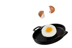 An image of an egg being cracked, falling, and transforming to fried egg on a black ceramic serving pan. Levitation food concept. 