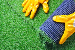 Hand of a worker in gloves with a artificial lawn grass. Artificial turf laying process. 