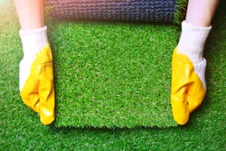 Greenering with an artificial grass background. Landscape designer holds a roll of an artificial turf in his hands. Image with a copy space. 