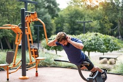 Hyperextension exercise. Charismatic man trains at the open air gym. Outdoor fitness background.
