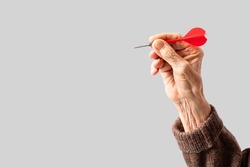 Wrinkled hand of an elderly woman takes aim at a target. Isolated on grey background.