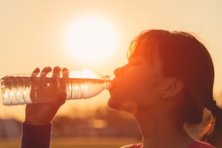 Female drinking a bottle of water. Closeup woman drinking a water on sunset. 