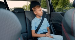 Little blond boy in a blue shirt opens passenger door in car, sits down and fastens his seat belt before starting the trip