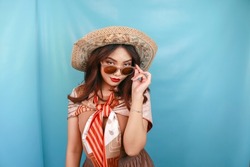 The traveling concept of a young Asian confident and happy woman is glancing and holding her sunglasses isolated by a blue background. 