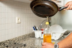 Man placing recycled edible oil from a frying pan into a plastic bottle in his home kitchen. Recycle at home concept. High quality photo