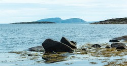 Northern calm seascape with rocky shore, boulders and seaweed. Sea islands and harsh northern nature. White Sea, Russia.