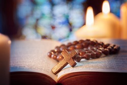 Rosary beads and crucifix cross on holy bible with candles in church