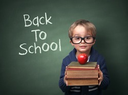Young child holding stack of books and back to school written on chalk blackboard