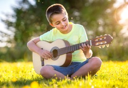Boy playing acoustic guitar in a summer field in the sunshine