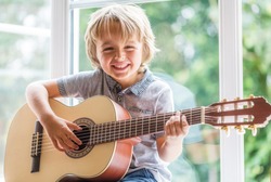 Happy smiling boy learning to play the acoustic guitar