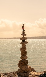 The art of stone balancing in the beautiful light of the sunset on the beach. A large pile of stones in perfect balance and above all is placed the statue of a geisha.